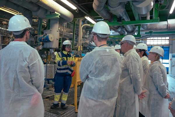  Image description: Group of workers wearing safety helmets and protective clothing listening to a colleague in an industrial facility